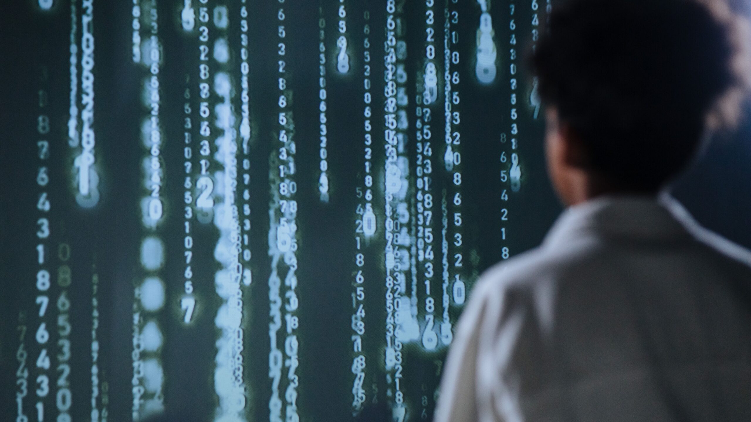 A person looking at a projection of numbers streaming down a wall.